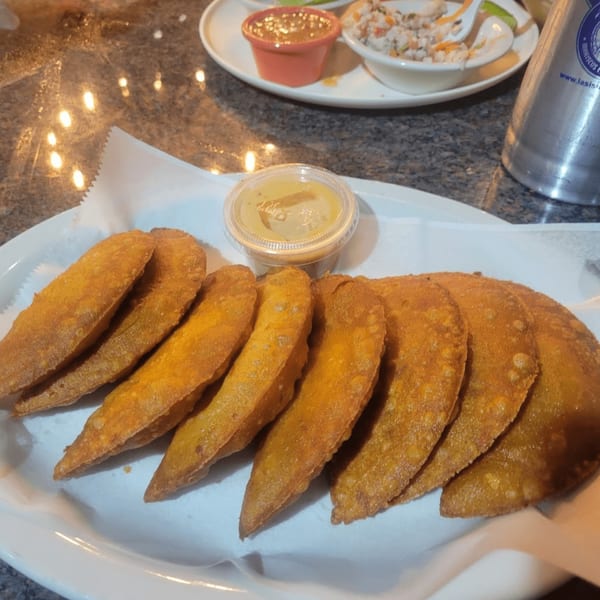 A plate of golden-brown empanadas with a side of dipping sauce at Las Islas VIP.