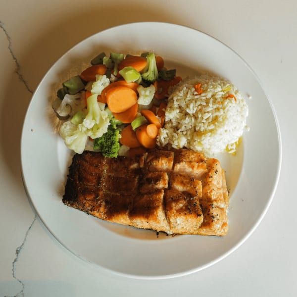 Grilled salmon fillet with a side of white rice and mixed steamed vegetables on a white plate.
