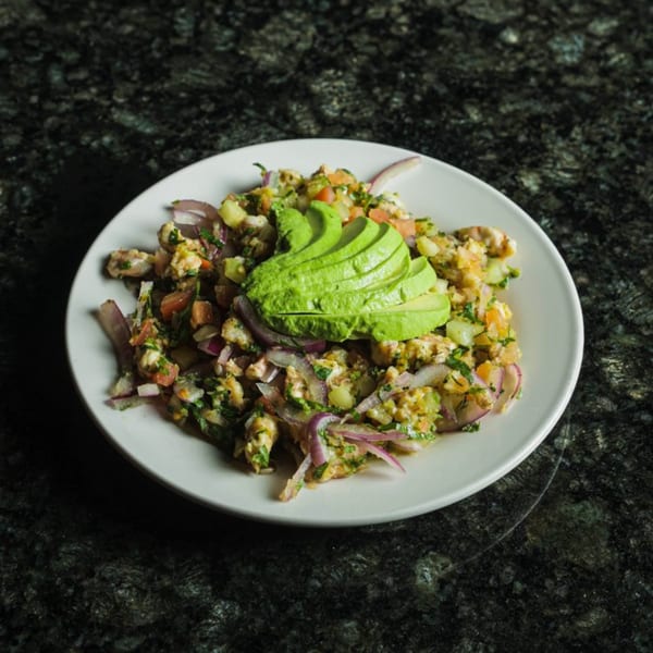 Las Islas VIP seafood ceviche with red onions, cilantro, and avocado slices on a white plate.