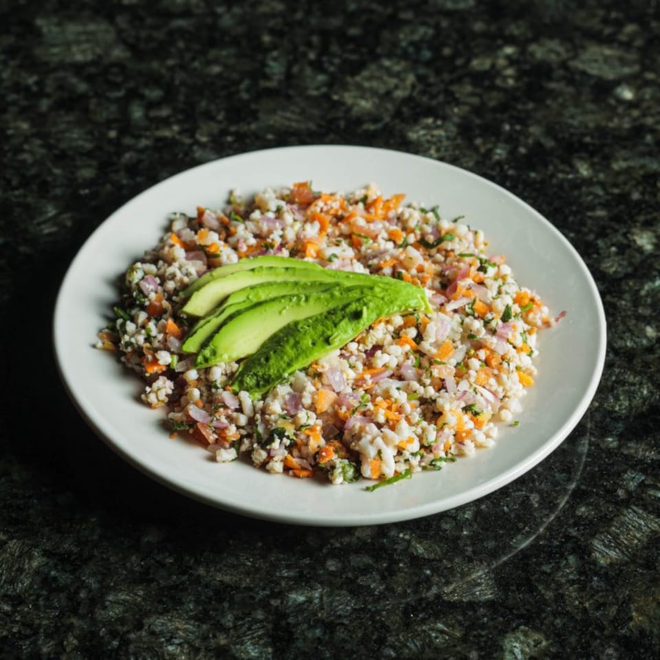 Seafood ceviche with diced red onion, carrots, and cilantro, topped with sliced avocado.