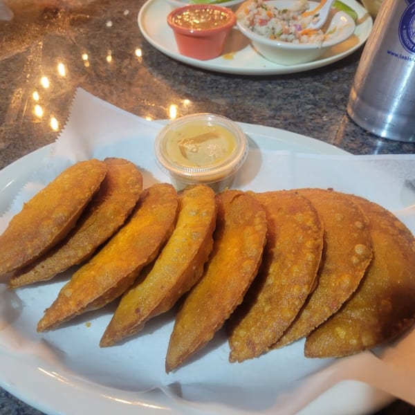 A plate of golden-brown empanadas with a side of dipping sauce, ceviche, and a drink.